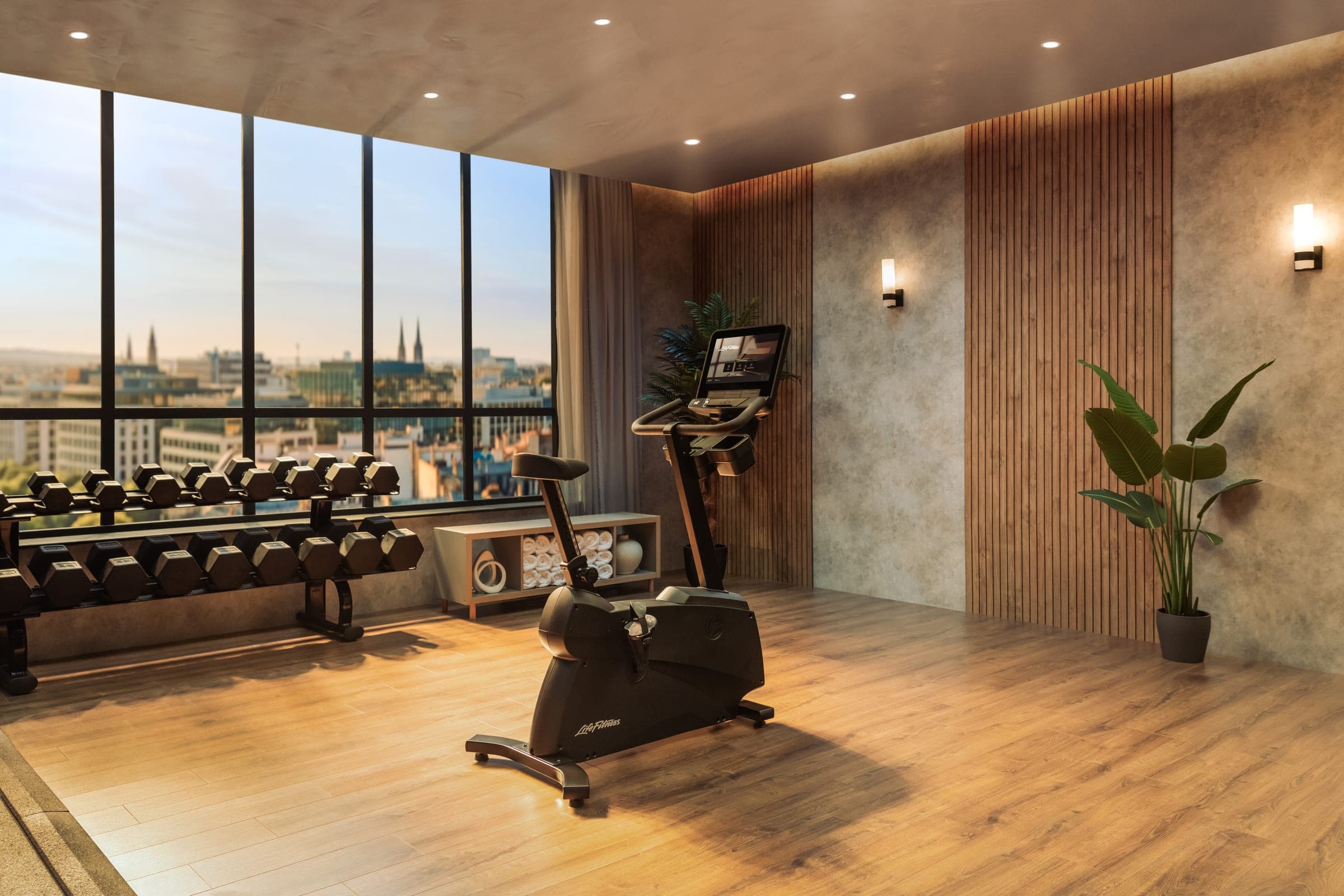 Fitness s rotopedem a činkami u prosklené stěny s výhledem na město, dřevěná podlaha a lamelové obložení