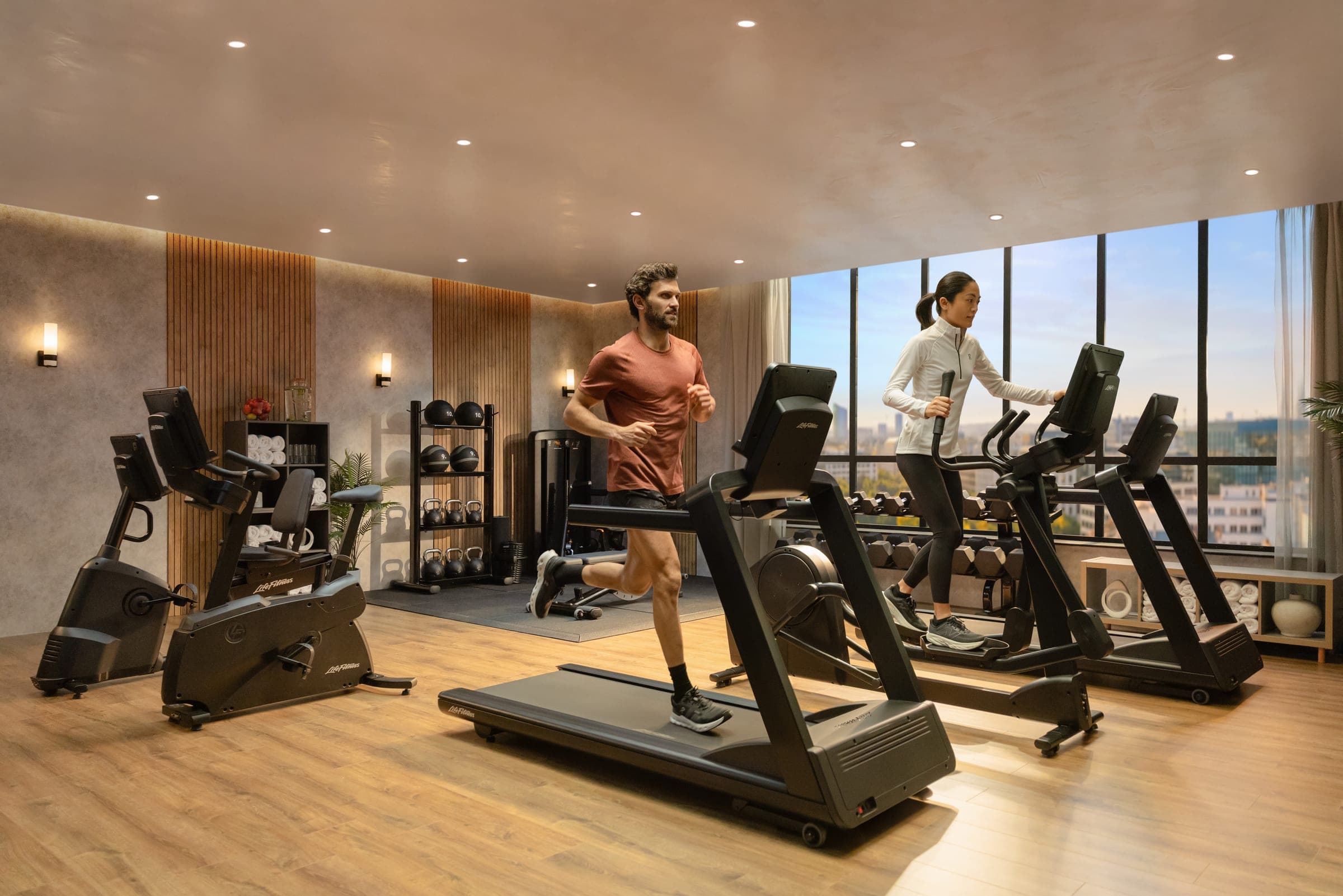 Hotelové fitness s výhledem na město, běžecký pás a eliptický trenažér u okna